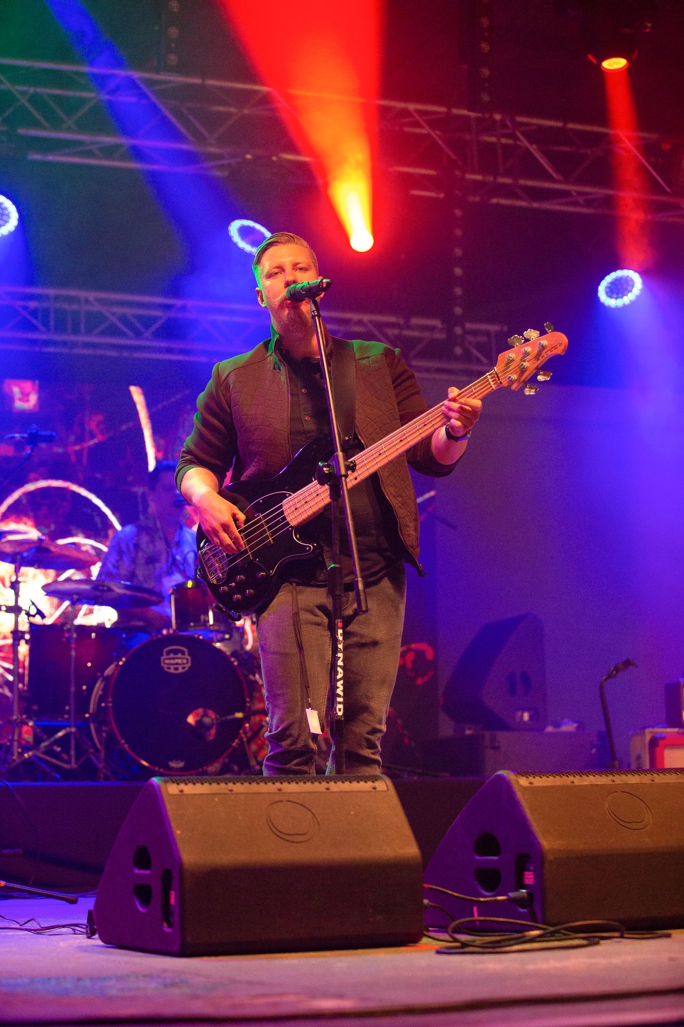 Basista Bigiel Band śpiewa na dużej scenie, nad nim kolorowe reflektory