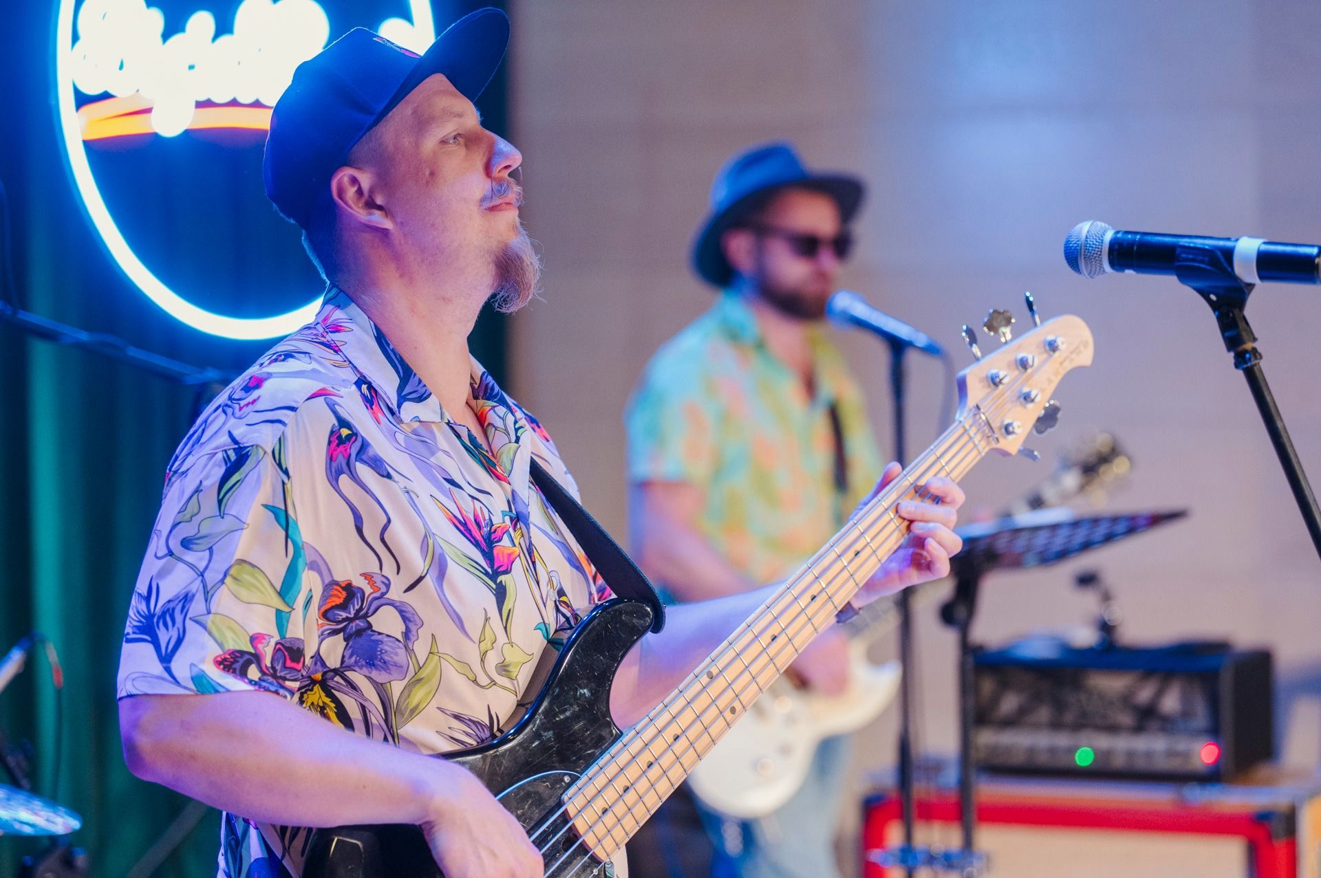 Basista Bigiel Band w kwiecistej koszuli gra na scenie, w tle neonowe logo zespołu