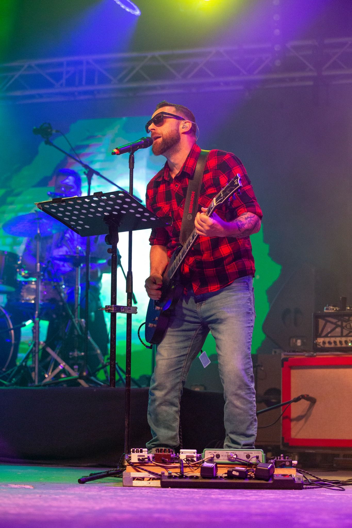 Gitarzysta Bigiel Band śpiewa na dużej scenie z kratownicą świateł i wzmacniaczami