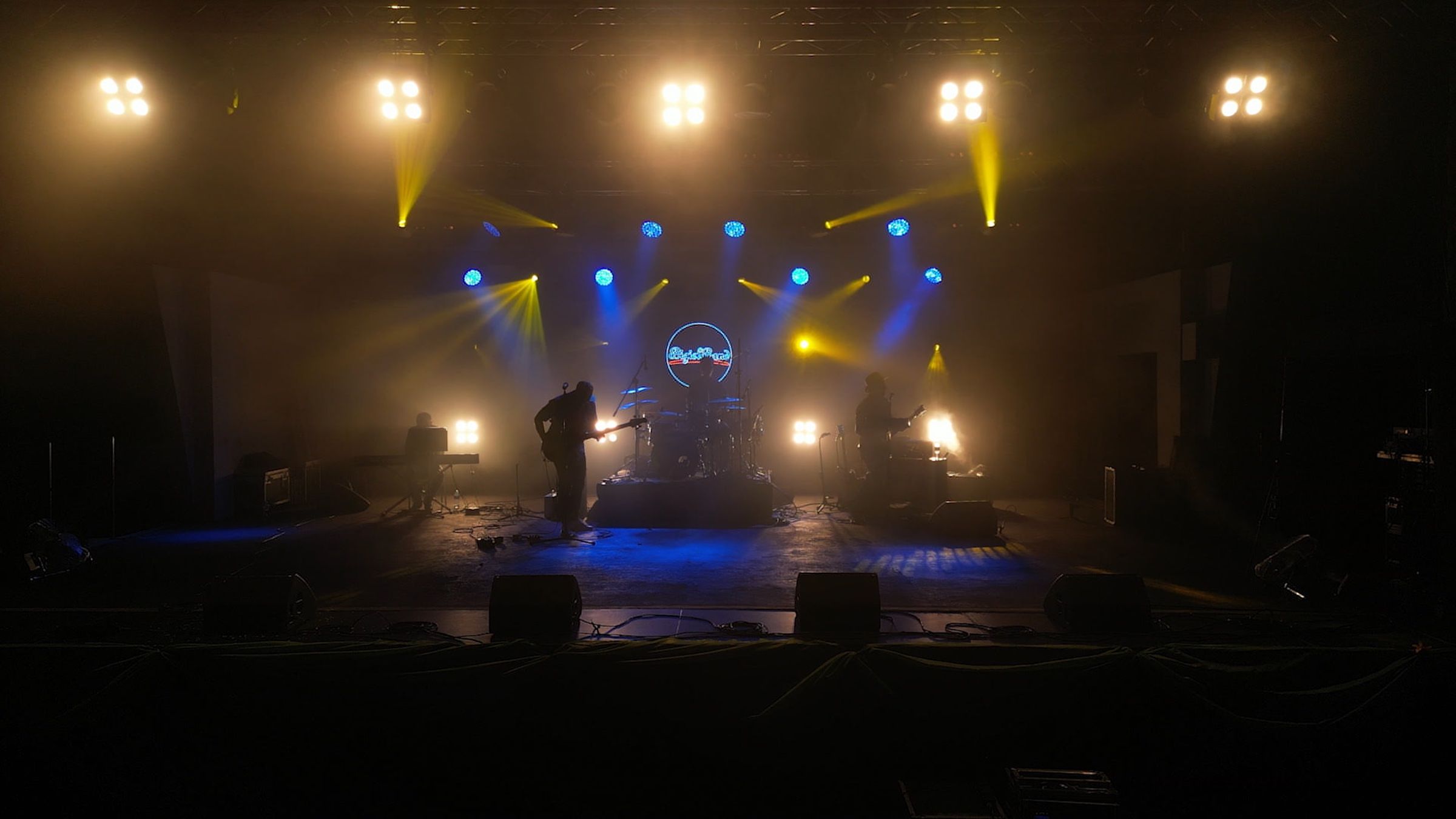 Bigiel Band na dużej scenie w snopach żółtego i niebieskiego światła, w centrum świeci neonowe logo zespołu