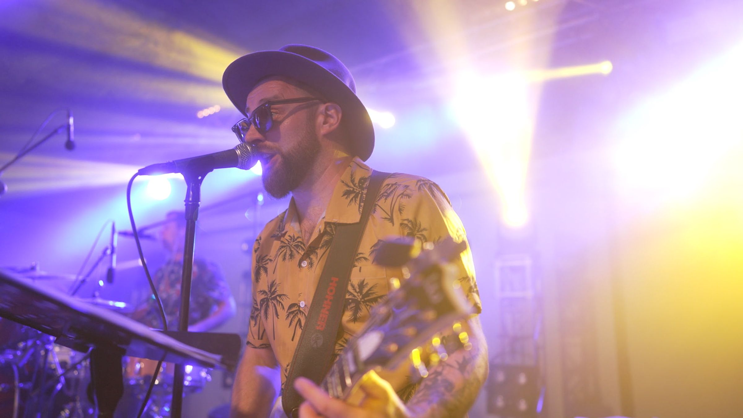 Wokalista Bigiel Band w kapeluszu śpiewa z gitarą w fioletowych i żółtych światłach sceny