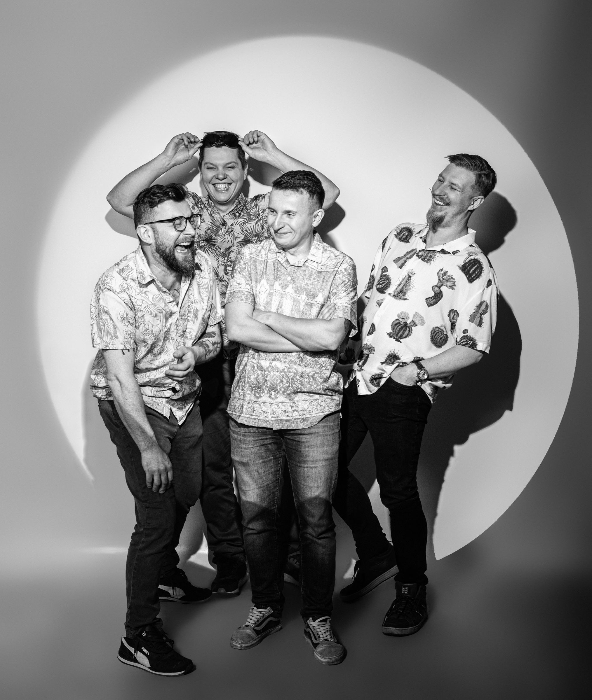 Czarno-białe zdjęcie czterech muzyków Bigiel Band śmiejących się w kręgu światła
